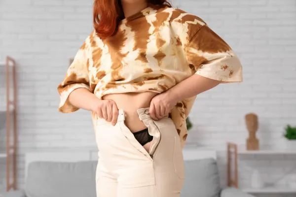 Image of woman trying to do her trousers up after pregnancy weight gain Huntingdon