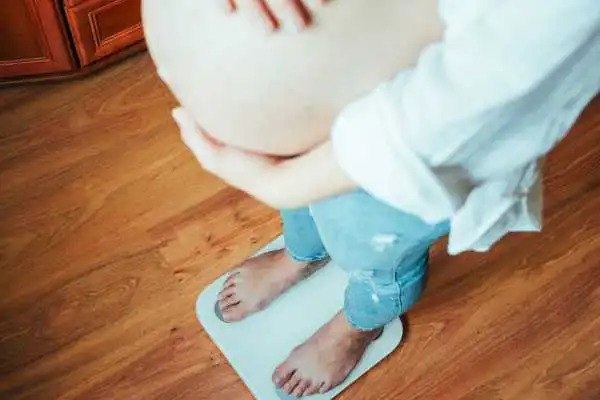 Image of woman weighing herself and experiencing weight gain through pregnancy Huntingdon